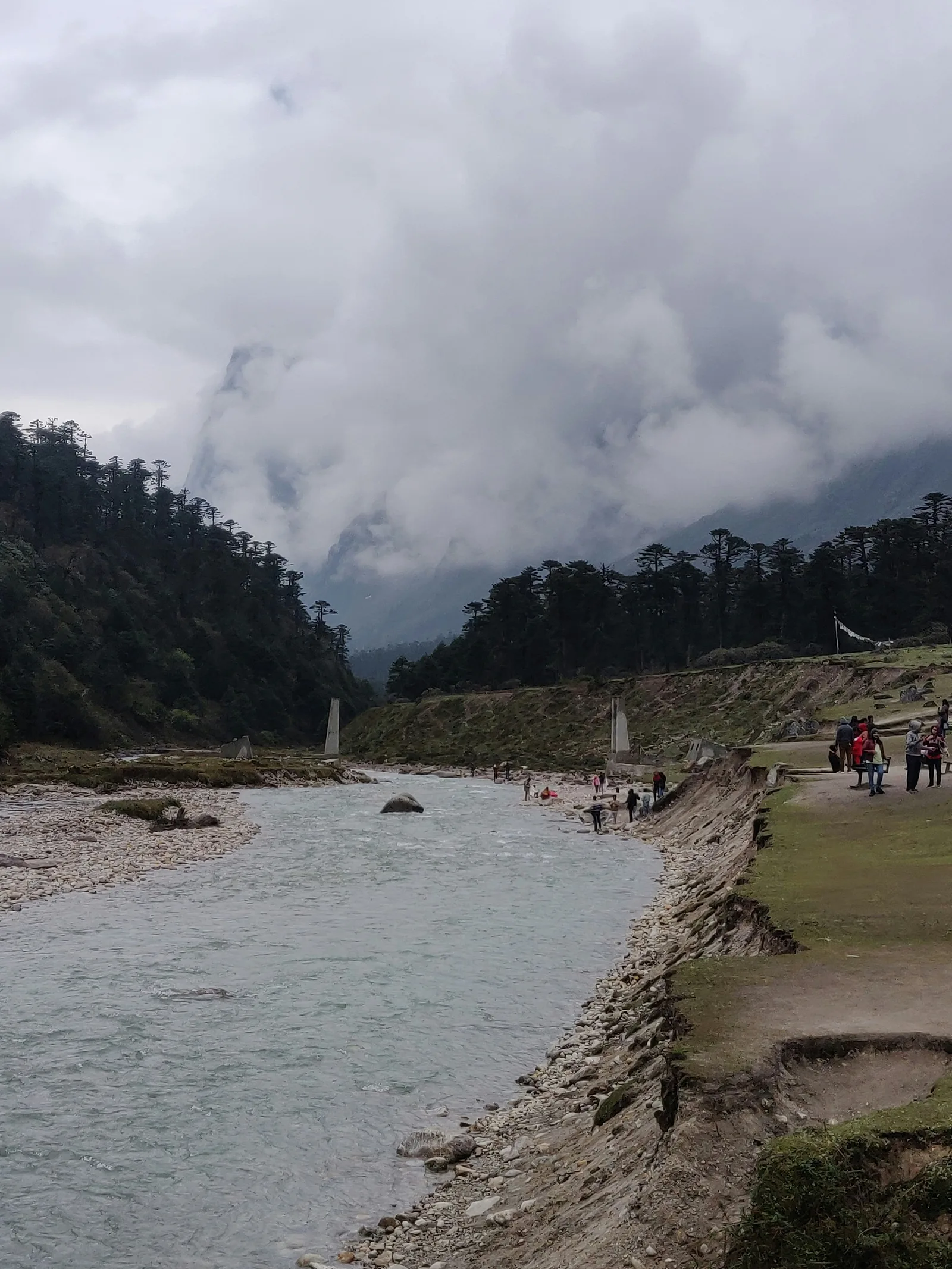 A wide river flowing through Yumthang Valley between mountains