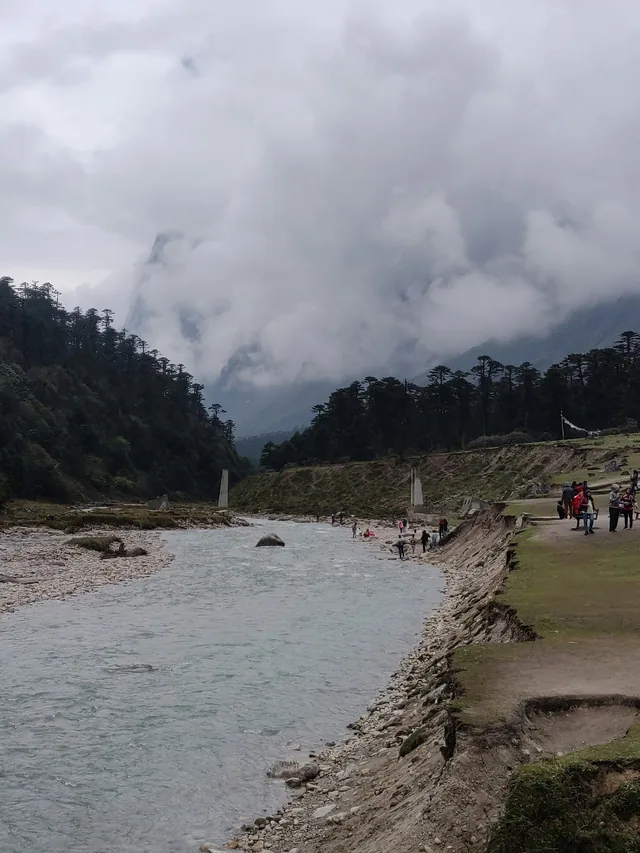 A wide river flowing through Yumthang Valley between mountains